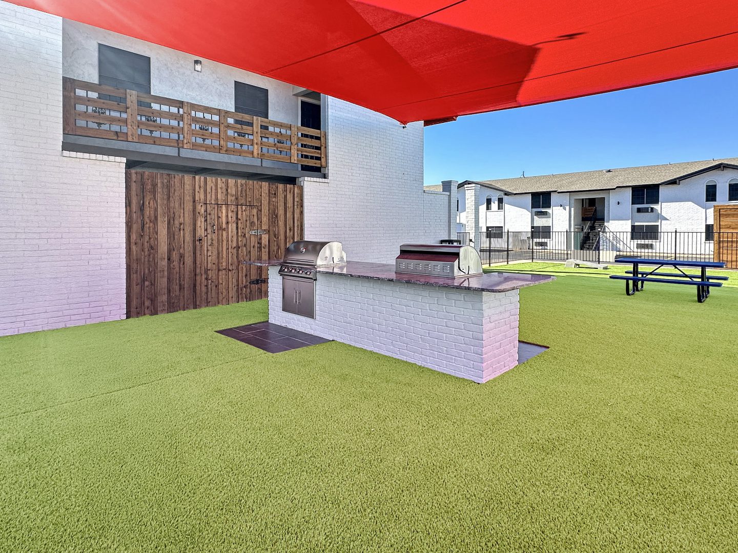 a patio with a grill and a red umbrella at The  Landing Apartments