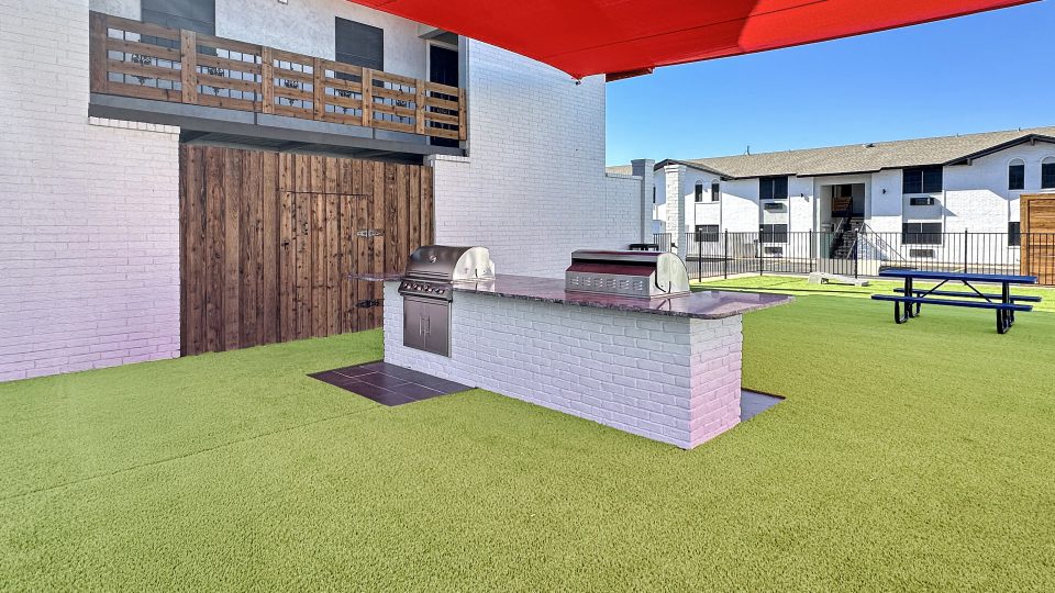 a patio with a grill and a red umbrella at The Landing Apartments