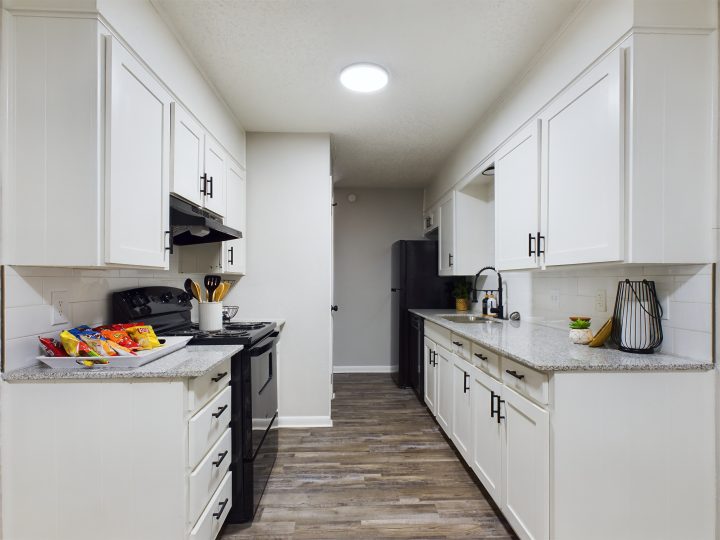 a long narrow kitchen with white cabinets and stainless steel appliances at The  Landing Apartments