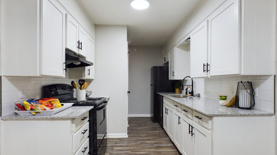 a long narrow kitchen with white cabinets and stainless steel appliances at The Landing Apartments